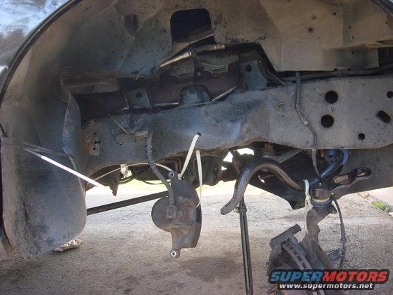 Undercarriage of a vehicle with suspension parts removed, showing the frame and brake components