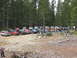 1979 Ford Bronco - Many off-road vehicles are gathered in a wooded area with people milling about.