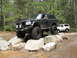 1979 Ford Bronco - Modified black Ford Bronco driving over rocks on a trail, with another Bronco behind it.