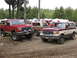 1979 Ford Bronco - Two Ford Broncos, one red and one red and tan, are parked on a gravel lot with trees and RVs in the background.