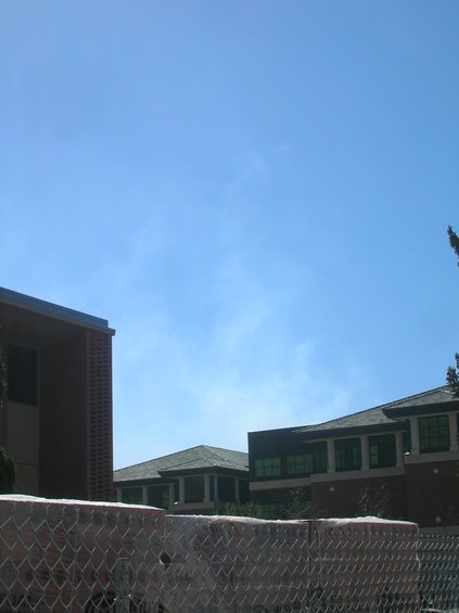 Buildings under a clear blue sky, with a chain-link fence in the foreground