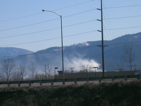 Smoke billows from a hillside with power lines and streetlights in the foreground