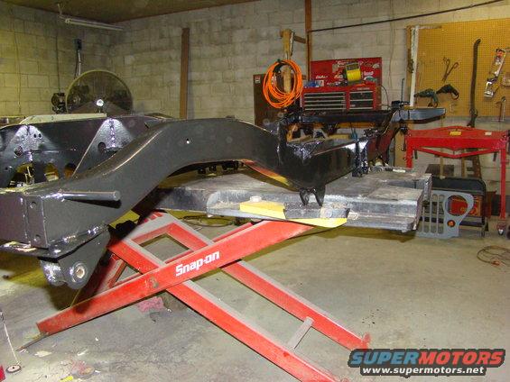 Vehicle frame on a red Snap-on lift in a garage. A Jeep grille is visible in the background