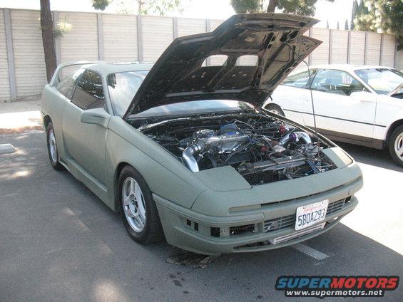 Car with hood open showing engine, another car behind it