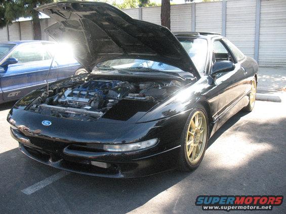 Black Ford Probe with gold wheels, hood open revealing engine, parked next to a blue car