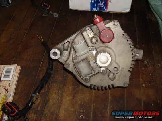 close-up of a car alternator with wiring harness attached, sitting on a wooden floor