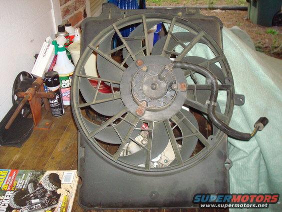 Radiator fan assembly with black blades and a central motor housing, resting on a green tarp