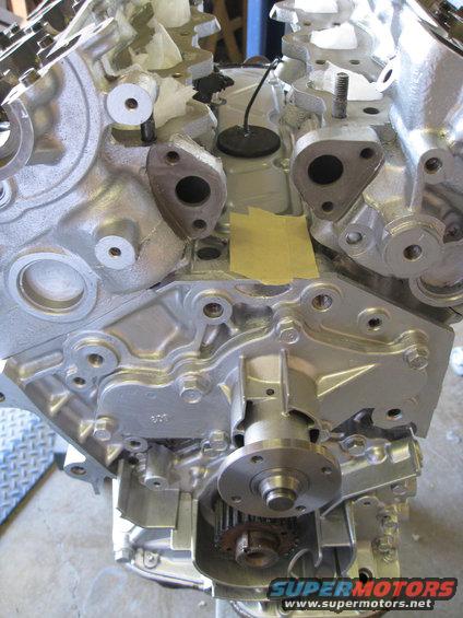 Silver engine block with water pump and timing gears visible. Yellow tape on the block