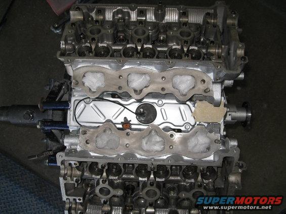 Engine block with intake manifold removed, showing gasket material and wiring. Supermotors.net logo visible