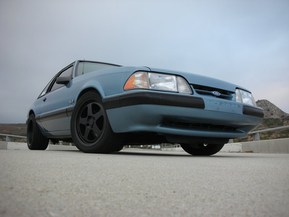 Blue 1990 Ford Mustang coupe with black wheels, viewed from a low angle