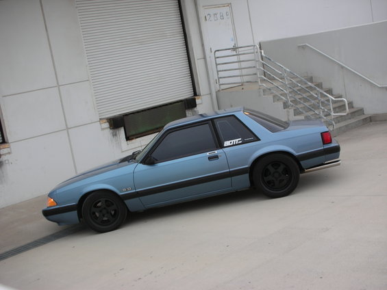 Blue 1990 Ford Mustang coupe with black wheels and a "5.0" badge