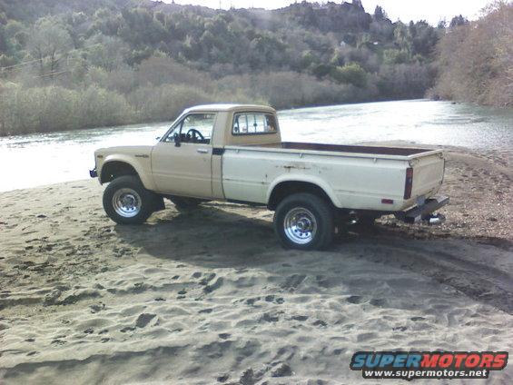 Tan and white pickup truck parked on sandy ground near a river