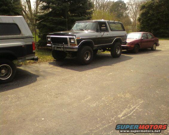 Ford Bronco towing a red sedan, parked next to another truck