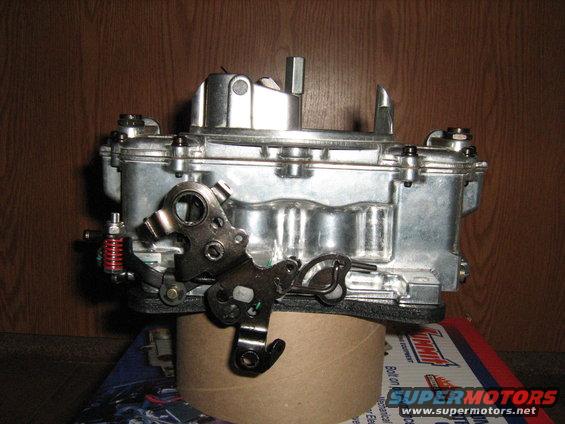 Chrome carburetor with linkage and red spring, resting on a cardboard tube
