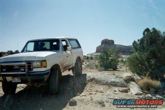 White Ford Bronco parked on rocky terrain with desert landscape and rock formations in background