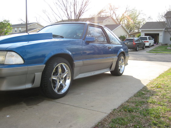 Blue and silver 1990 Ford Mustang with aftermarket hood scoop and chrome wheels parked on a driveway