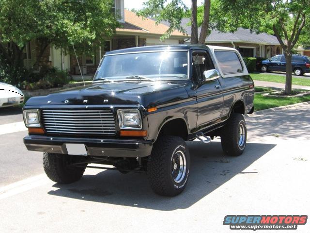 Black Ford Bronco with a white top, lifted on large tires, parked in a suburban driveway