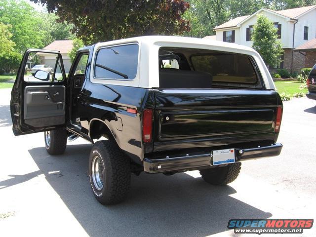 Black 1978 Ford Bronco with white top, rear view, driver's door open, parked on asphalt