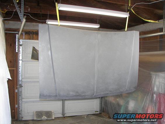 Gray car hood hanging in a garage, suspended by yellow straps