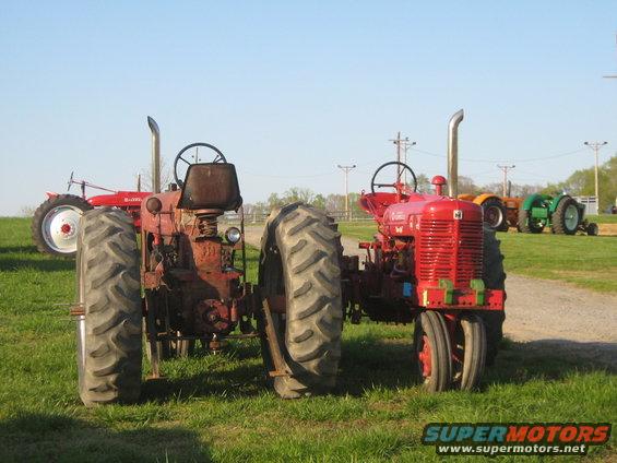 Two red tractors parked on grass, one in foreground with large rear tires and exposed engine