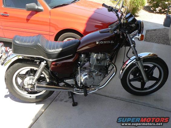 Side view of a maroon Honda motorcycle parked next to a red car
