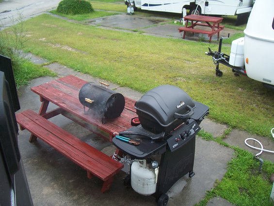 Black Char-Broil grill and small smoker on red picnic table, with propane tank