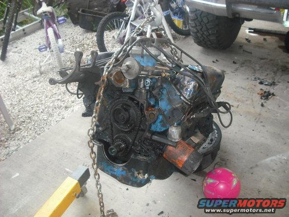 Engine block suspended by chains, resting on an engine stand. A pink ball is on the ground nearby