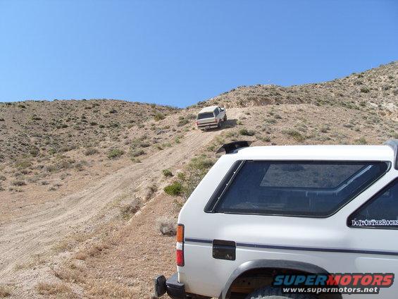 White SUV with a sunroof driving on a dirt hill, rear view