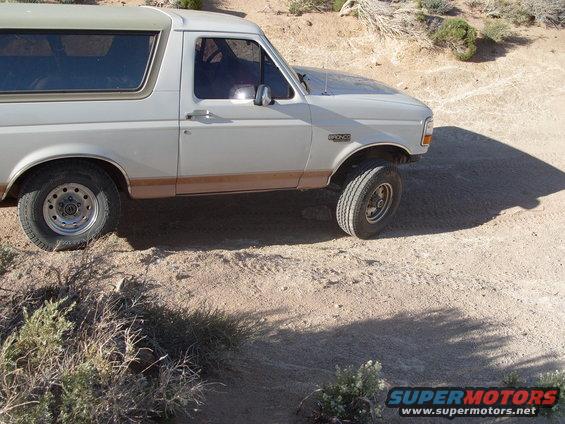 White Ford Bronco parked on a dirt road with scrub brush