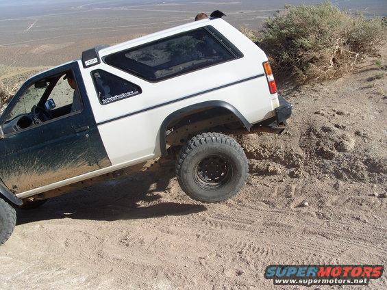 Two-tone SUV with off-road tires climbing a dirt hill. Sticker on door reads 'DirtCoversTheRest.com'