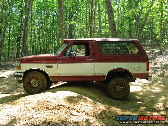 Two-tone red and white Ford Bronco with off-road tires parked on a dirt path