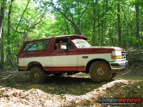 Red and white Ford Bronco driving on a dirt trail in the woods