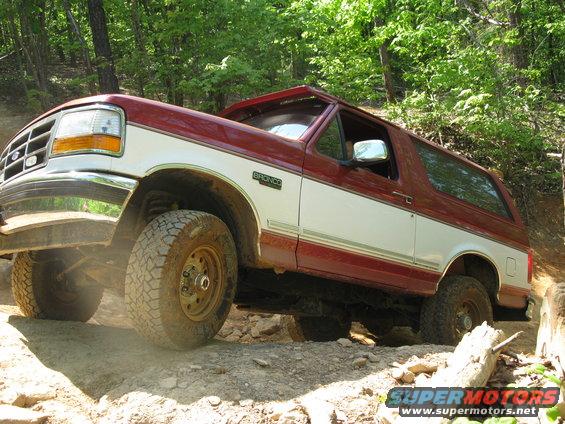 1995 Ford Bronco climbing a rocky hill, red and white paint, off-road tires