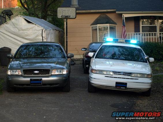 Front view of two 1999 Ford Crown Victorias, one a police car with lights on