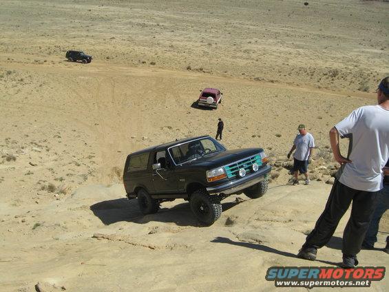 Black Ford Bronco navigating rocky terrain with two people watching