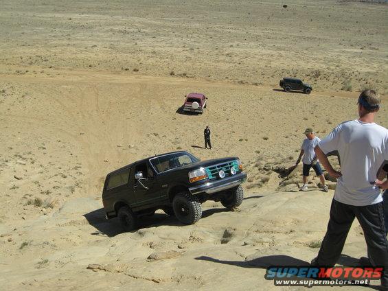 Black Ford Bronco climbing rocky terrain, green grille, auxiliary lights