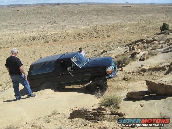 Black 1993 Ford Bronco navigating a rocky off-road trail with two people nearby