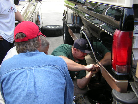 Three men working on the side of a black SUV with a tan stripe. A spare tire is visible in the background
