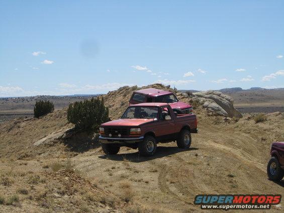 Red 1993 Ford Bronco parked on a dirt hill with a pink Ford Bronco behind it