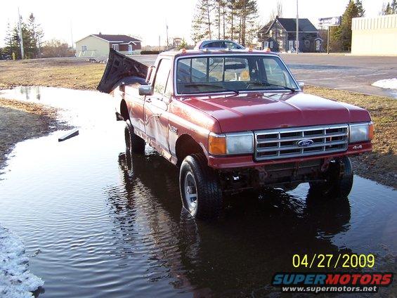 Red pickup truck parked in a large puddle, hood is open and propped up