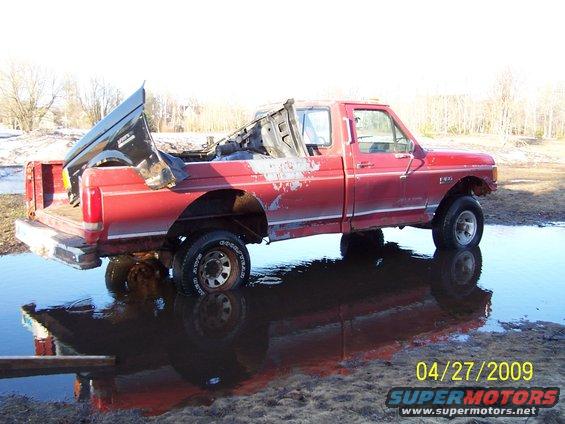 Red 1989 Ford F-150 in water, side view, damaged bed