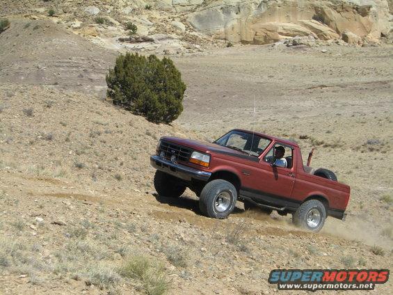 Red 1993 Ford Bronco driving off-road on a dusty hill