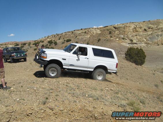 White Ford Bronco driving on a dirt hill with a black Ford Bronco behind it