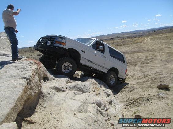 White 1993 Ford Bronco climbing over large rocks on an off-road trail