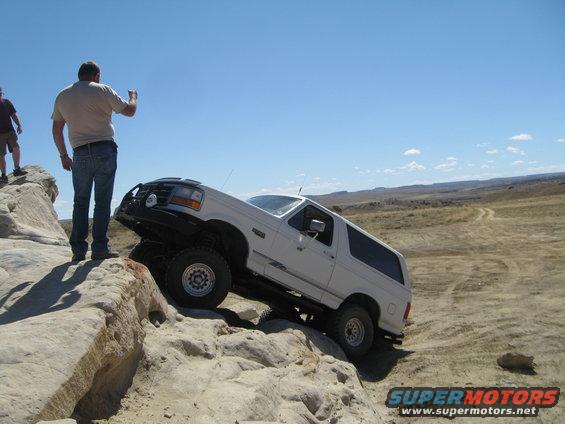 White 1992 Ford Bronco climbing a rocky incline with two men watching