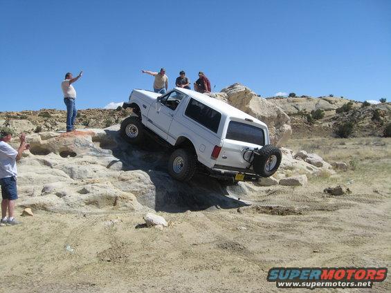 White 1993 Ford Bronco climbing over rocks with people watching