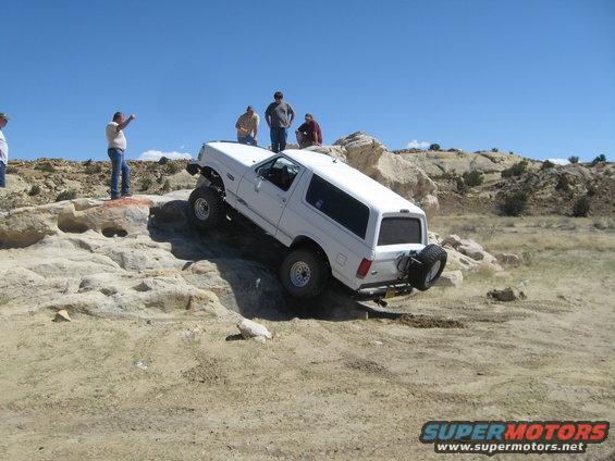 White Ford Bronco climbing rocks, spare tire on rear, people watching
