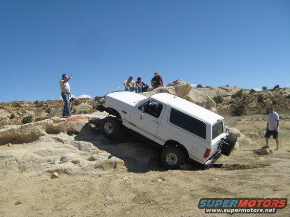 White 1993 Ford Bronco navigating rocky terrain with people watching