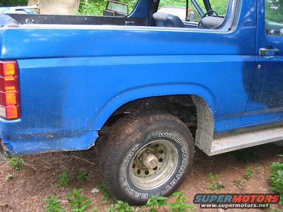 Blue Ford Bronco rear quarter panel, showing the wheel well, tire, and diamond plate step. The tire reads 'Wild Country Radial XRT'