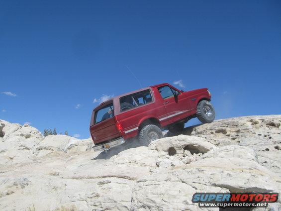 Red SUV climbing a rocky hill under a clear blue sky
